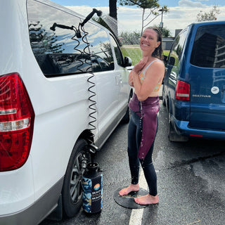 Woman using Beach Soul portable shower for outdoor rinsing beside a vehicle