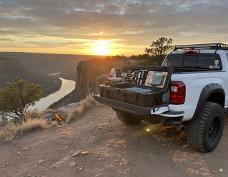 VOZ portable camp kitchen set up on a pickup truck tailgate at a scenic river canyon campsite at sunset