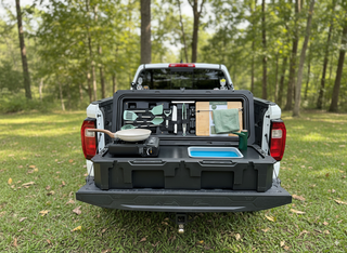 VOZ portable camp kitchen open on a pickup truck tailgate with cooking station, sink and organized accessories