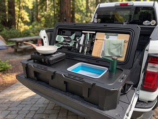 VOZ portable camp kitchen with sink and cooking station set up on a pickup truck tailgate at a forest campsite